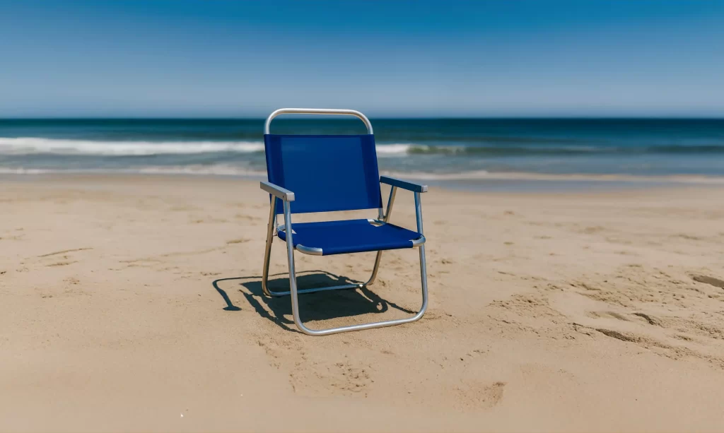 Cadeira de praia azul com estrutura metálica posicionada na areia, em frente ao mar com céu azul claro ao fundo